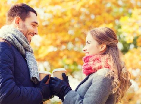 Smiling couple with coffee cups in autumn park