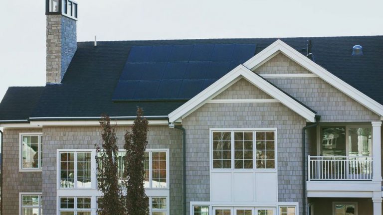 Solar Panels on a large seaside home with chimney and many windows.