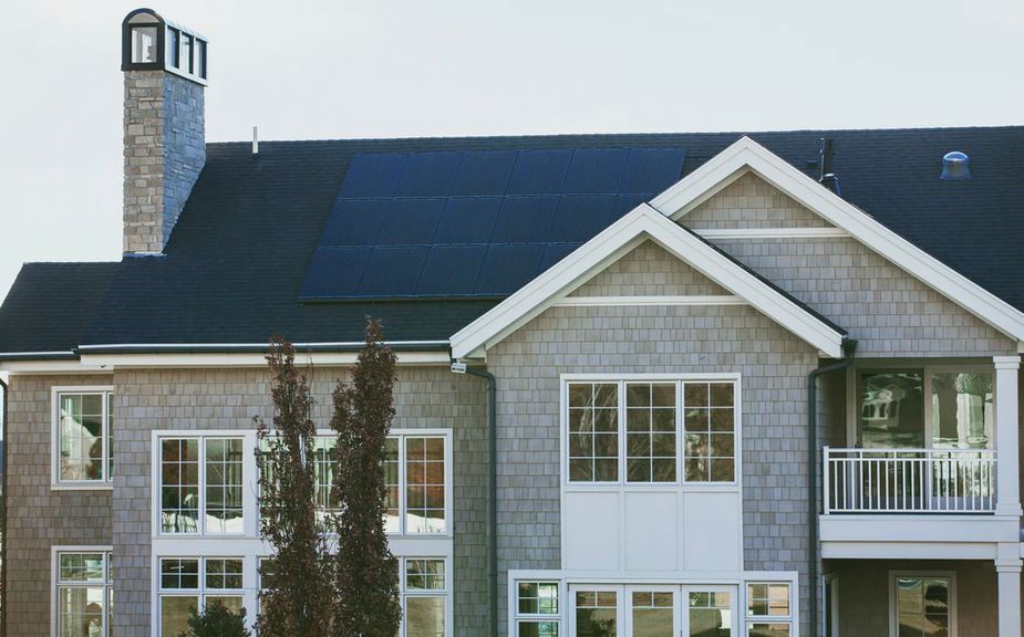 Solar Panels on a large seaside home with chimney and many windows.