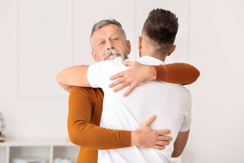 Senior man and his adult son hugging at home