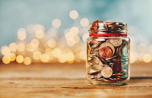 Donation money jar filled with coins in front of holiday lights teach your kids about money management,