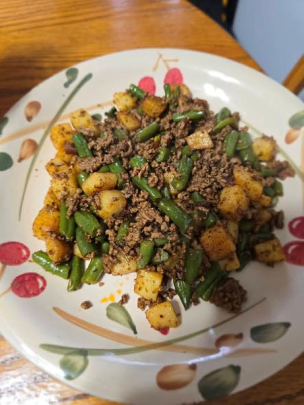 serving of beef and bean hash on a white ceramic plate with a cherry and leaf pattern, showcasing the crispy potatoes and lean beef.