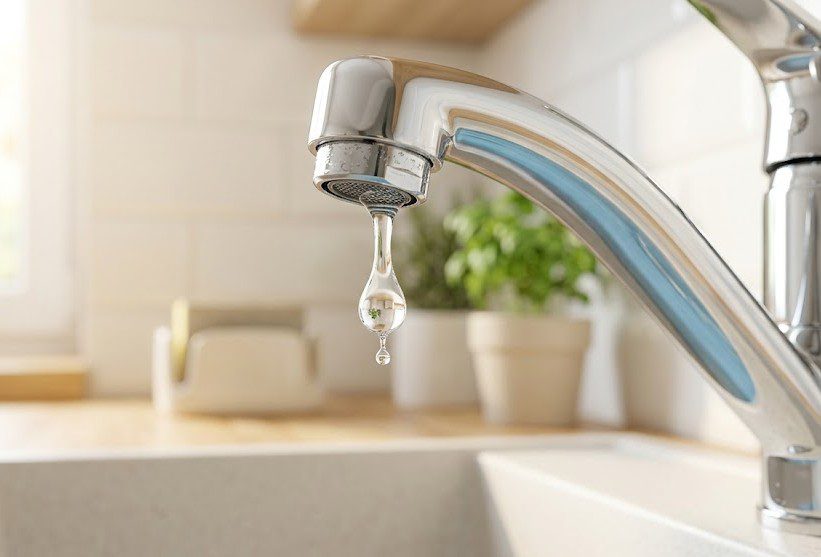 A close-up of a modern silver faucet with a single water drop about to fall, highlighting water conservation and home maintenance.