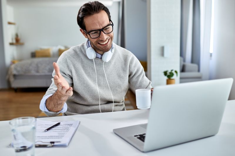 young happy businessman drinking coffee using computer while having video conference home Growing Remote Business? Make Sure Your Employees are Safe and Efficientcoffee using computer while having video conference home