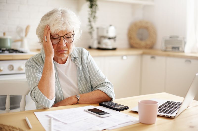 sad frustrated senior woman pensioner having depressed look holding hand her face calculating family budget sitting kitchen counter with laptop papers coffee calculator cell phone Financial Planning After Divorce Over 50: Your New Life