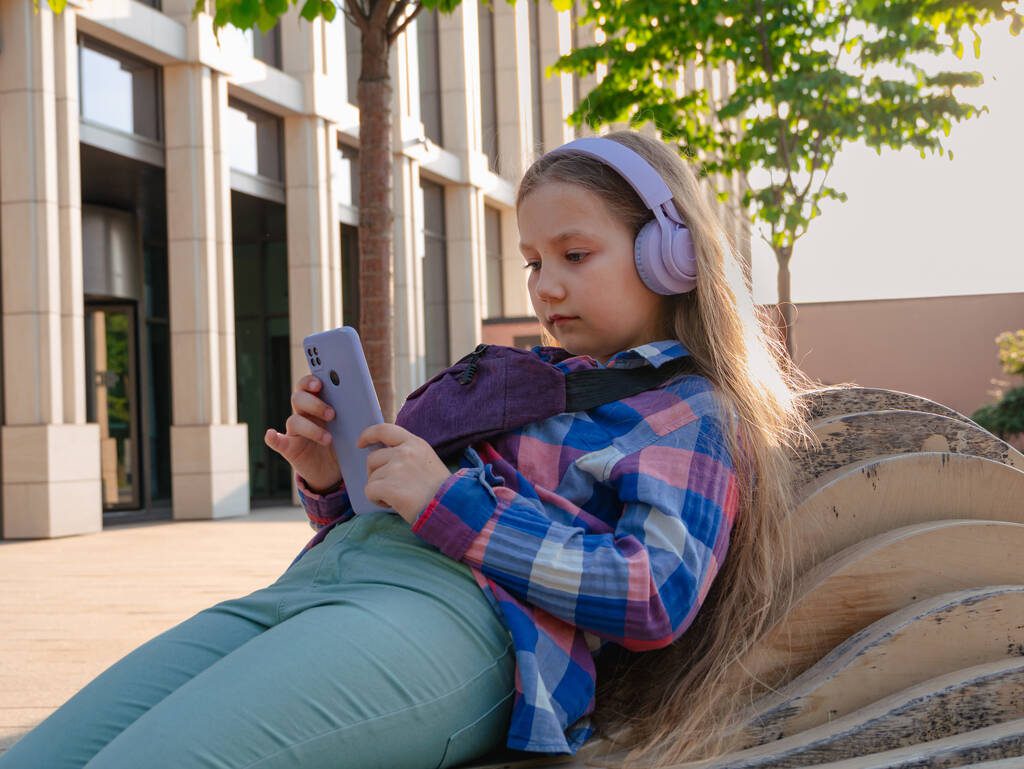 stock photo blonde child purple headphones listening music podcast using smartphone bench Auditory Memory Learning Aids for Kids & Comprehension Skills