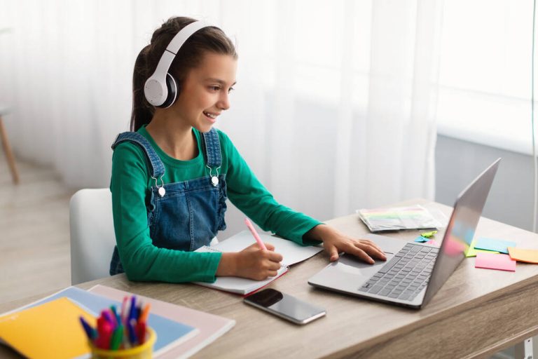 stock photo girl sitting at desk using laptop writing in textbook
